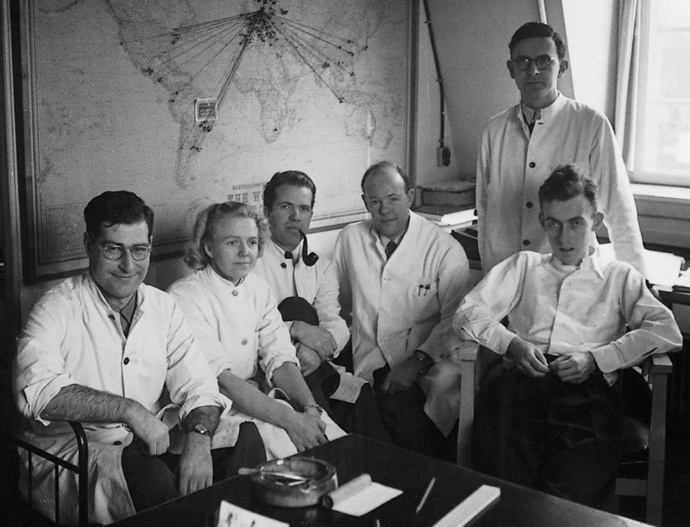 Niels Jerne standing beside a window behind five seated colleagues at Statens Serum Institut in 1950.