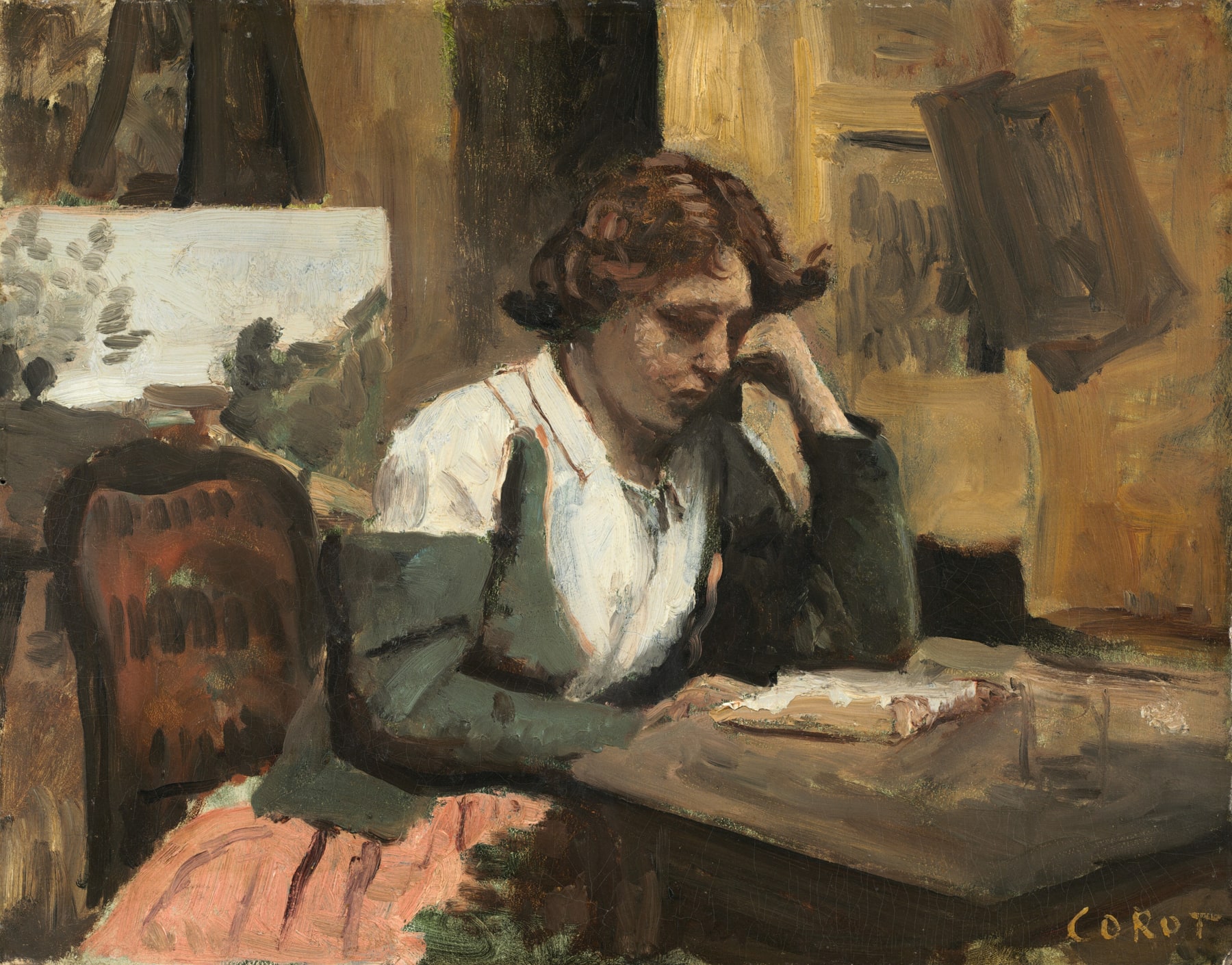 A woman rests her head on one hand as she reads a book at a table in an artist’s studio.